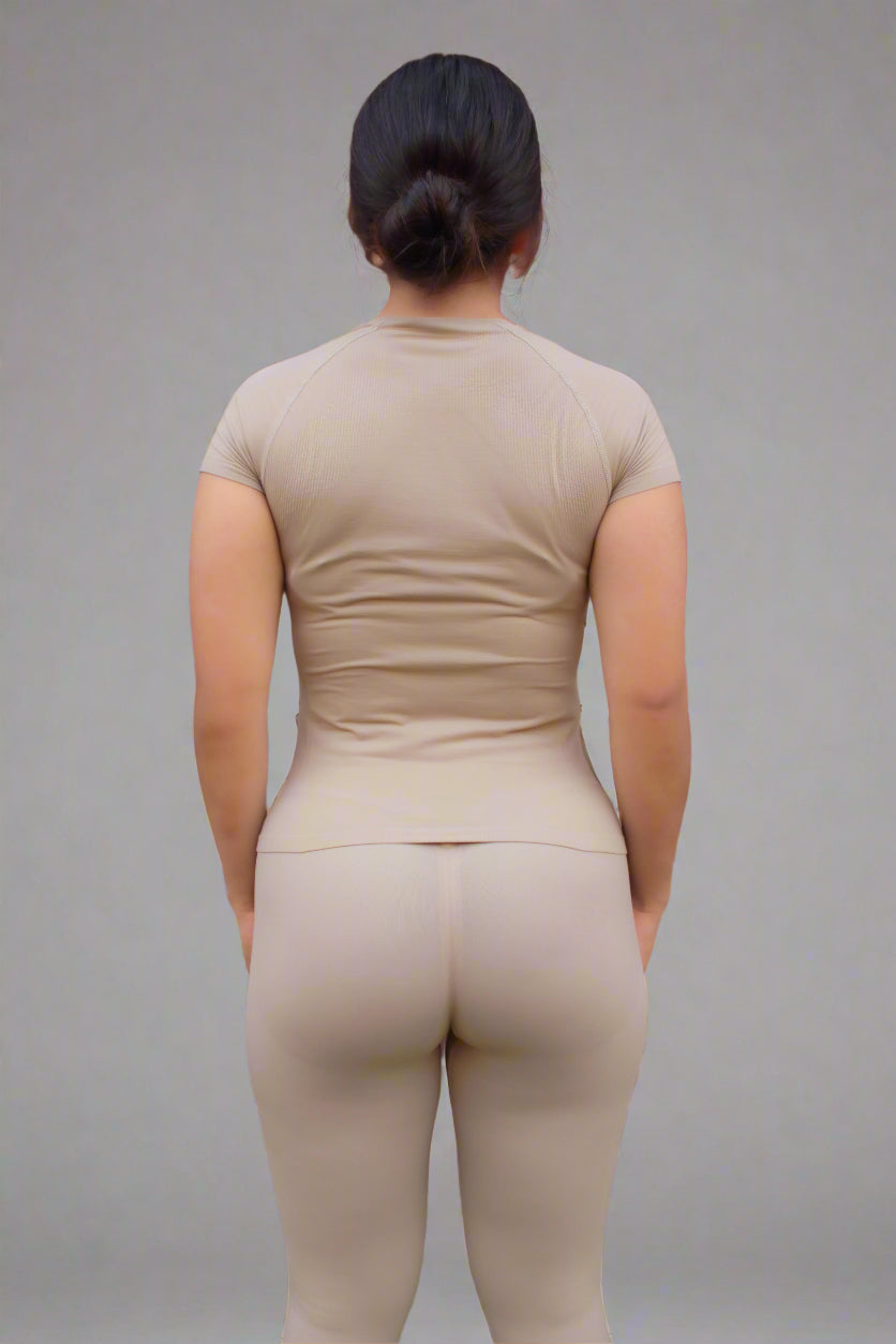 Person wearing a beige outfit standing against a brick wall.