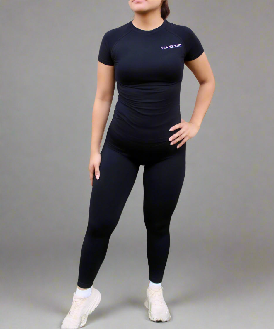 woman wearing black activewear fitted top with leggings and beige tennis shoes with a brick wall background