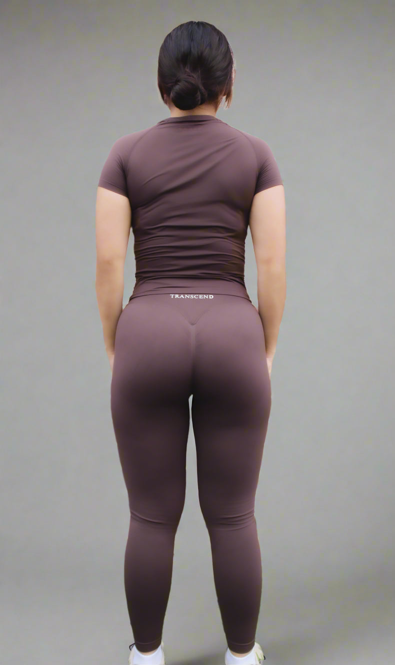 woman wearing brown activewear fitted top and legging with logo facing brick wall