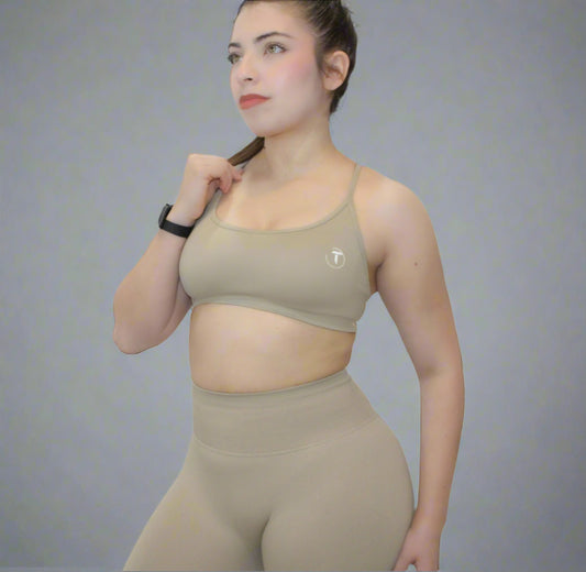 Woman wearing a beige sports bra and leggings on a plain background