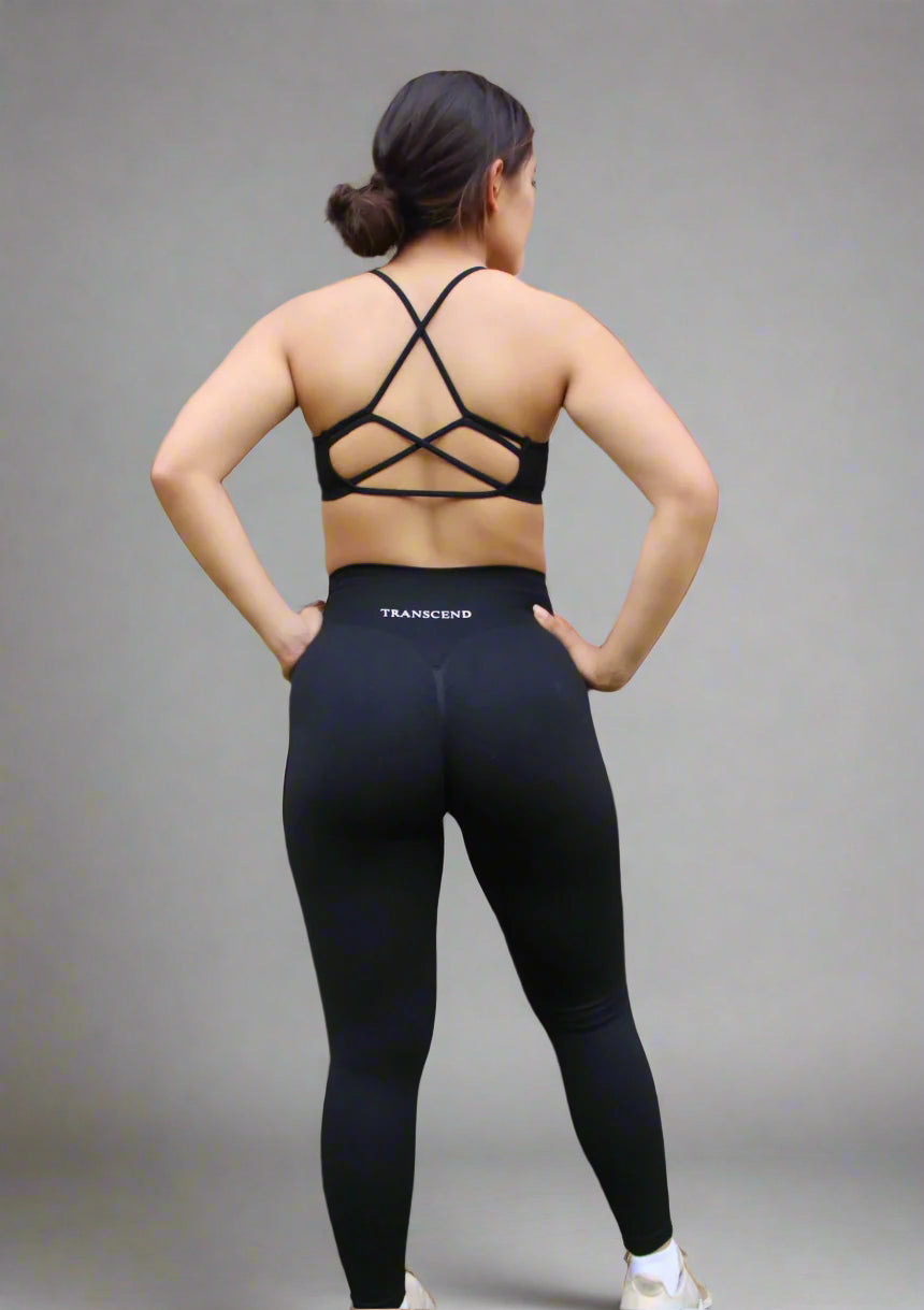Person wearing black sports bra and black athletic leggings with 'Transcend' branding in front of a brick wall.