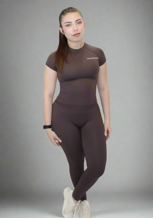 Woman wearing a brown athletic outfit with 'TRANSCEND' branding on a light gray background