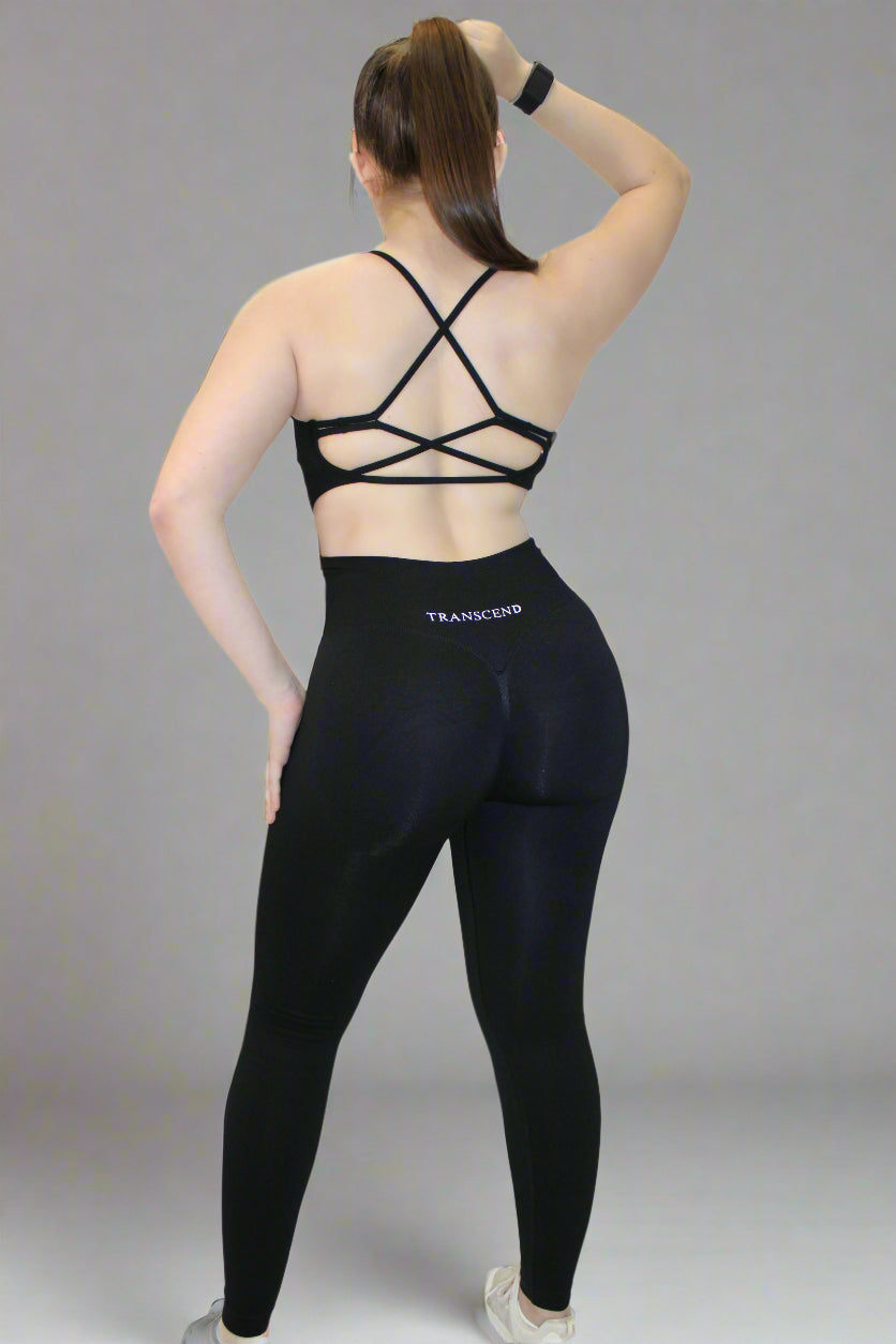 Person wearing black athletic bra and leggings with 'TRANSCEND' branding on a white background